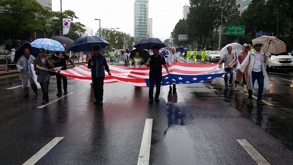 광복절에 대한민국의 독립에 큰 기여를 한 미국 성조기가 빠질 수 없다. 빗속에서 한손에는 우산을, 한손에는 대형 성조기를 나눠들고 행진하는 참가자들. 사진 = 애국시민 민병일님의 페이스북. 